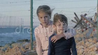 沮丧的孩子。 孤独的女孩在悲伤的男孩身边哭泣。 悲伤的小难民兄弟姐妹在州城附近的岸边